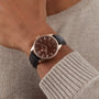 A person wearing the William Wood Chivalrous Collection - Chocolate watch with a black leather strap and a beige knit sweater.
