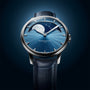 The Arnold & Son Perpetual Moon 41.5mm Platinum features a blue dial, moonphase display, and a dark blue leather strap, set against a blue background.
