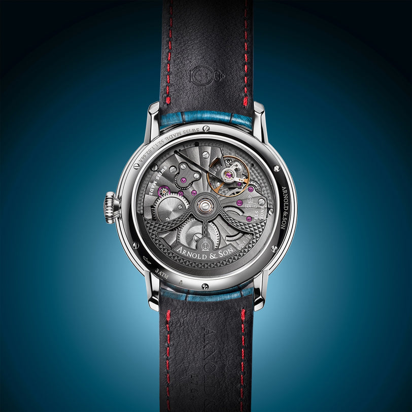 The Arnold & Son Globetrotter Steel is a luxury watch featuring visible gears, a black leather strap, and set against a blue gradient background.