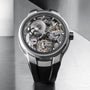 A close-up of the Greubel Forsey Tourbillon 24 Secondes Architecture, featuring its exposed mechanical movement, visible gears, and black strap against a metallic background—showcasing its architectural tourbillon design.