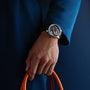 A person in a blue coat showcases the Greubel Forsey Tourbillon Cardan, its exposed movement visible as they hold an orange cable—highlighting the watchs high-end craftsmanship and exceptional quality.