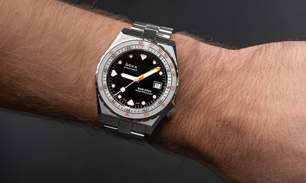 A wrist wears the DOXA Sub 600T watch with a black dial and silver-tone strap