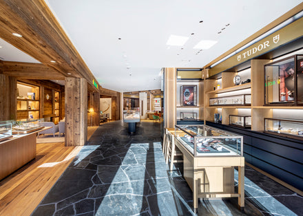 Luxury watch store with glass display cases, wooden accents, and Tudor brand signage on the wall.
