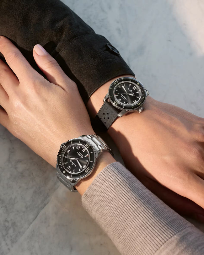 Two divers wearing 42.3mm watches with sunburst black dials, rotating bezels, and rubber straps on their wrists.