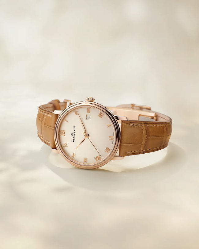 Rose gold-toned watch with cream dial, Roman numerals, and tan crocodile-textured leather strap.