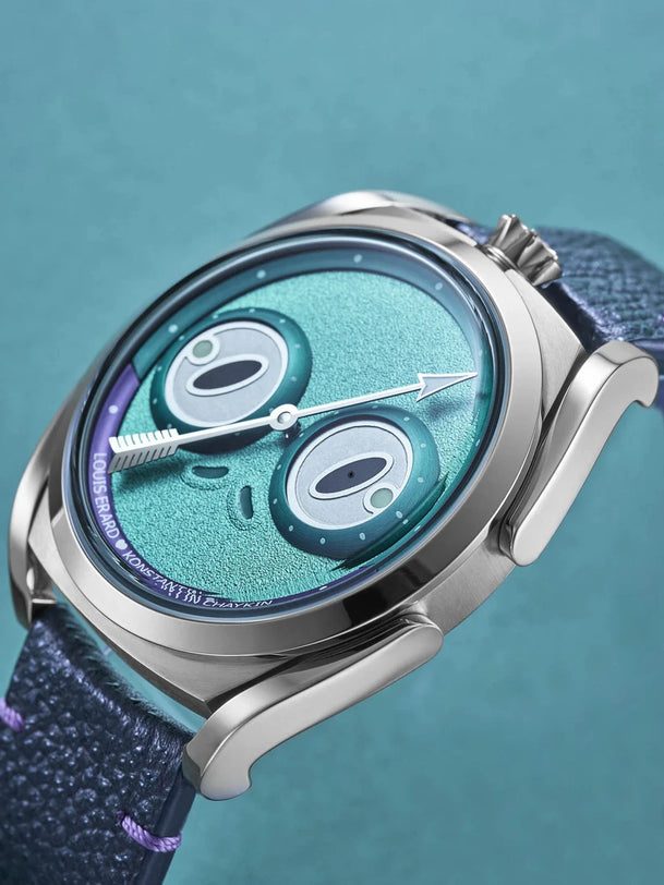 Titanium watch with turquoise dial featuring frog-shaped subdials, arrow hands, and blue fabric strap on turquoise background