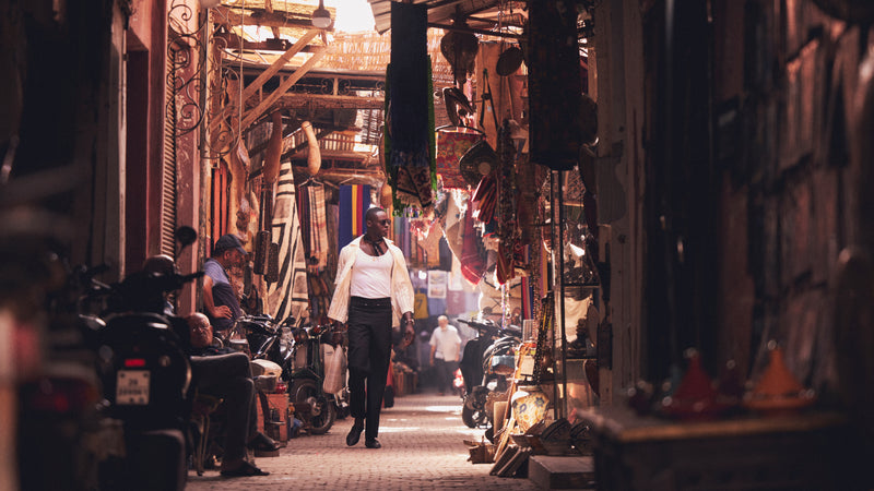 Roze Traore walks through a crowded bazaar wearing a white shirt and undershirt and black pants
