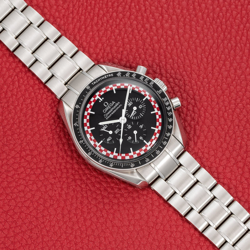 An OMEGA Speedmaster Tintin watch with a black dial and silver case displayed on a red textured background.
