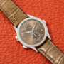 A Patek Philippe Calatrava Travel Time Ladies watch featuring a diamond bezel and leather strap is displayed on textured orange leather.