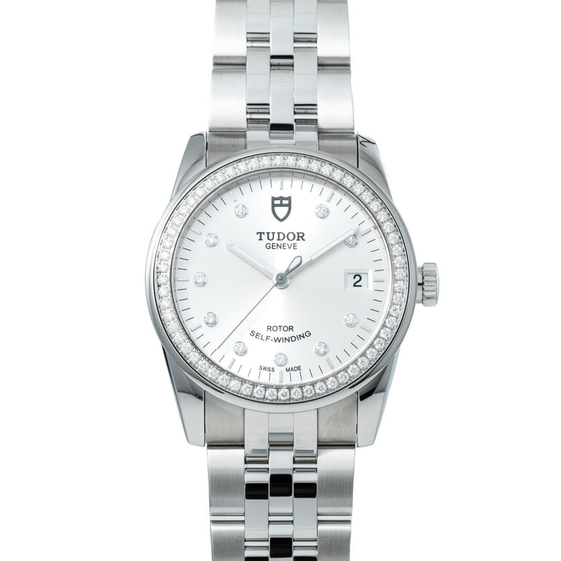 The TUDOR Glamour Date wristwatch features a silver-tone case, white dial with diamond markers, date display, and a metal bracelet.