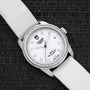 The TUDOR Glamour Date wristwatch features a white strap and diamond bezel, showcased on a textured black surface.