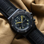 The Audemars Piguet Royal Oak Offshore End of Days chronograph watch features yellow accents on a black strap, displayed on tan fabric.
