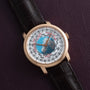 The Vacheron Constantin Traditionnelle World Time, featuring a brown leather strap, is showcased on a textured dark purple surface.