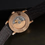 Close-up of the Vacheron Constantin Traditionnelle World Time watch back, featuring its intricate gold movement and a brown leather strap.