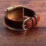 The Birks Rectangular Dress Watch by Patek Philippe, featuring brown leather and a gold buckle, is displayed on a wooden surface.