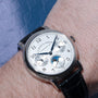 A Lange & Sohne Lange 1815 Annual Calendar silver wristwatch with a black leather strap, featuring moon phase and date dials on the wearer’s wrist.