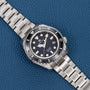 A Grand Seiko Hi-Beat Professional 600m Divers Limited Edition silver watch with a black bezel rests on a blue textured surface.