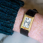 The Cartier Tank Basculante Mécanique 150th Anniversary Limited Edition is a gold rectangular wristwatch with Roman numerals on a brown leather strap, shown worn on a person’s wrist.