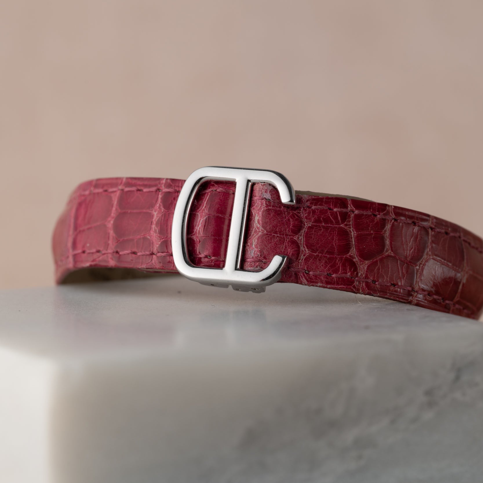 A Cartier Cle de Diamond red crocodile leather belt with a silver CC buckle displayed on a white marble surface.