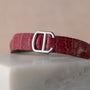 A Cartier Cle de Diamond red crocodile leather belt with a silver CC buckle displayed on a white marble surface.