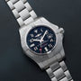 A Breitling Avenger II Seawolf with a stainless steel case, blue dial, and metal bracelet rests on a black surface.