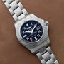A Breitling Avenger II Seawolf stainless steel watch with a blue dial, date window, and metal bracelet displayed on a brown surface.