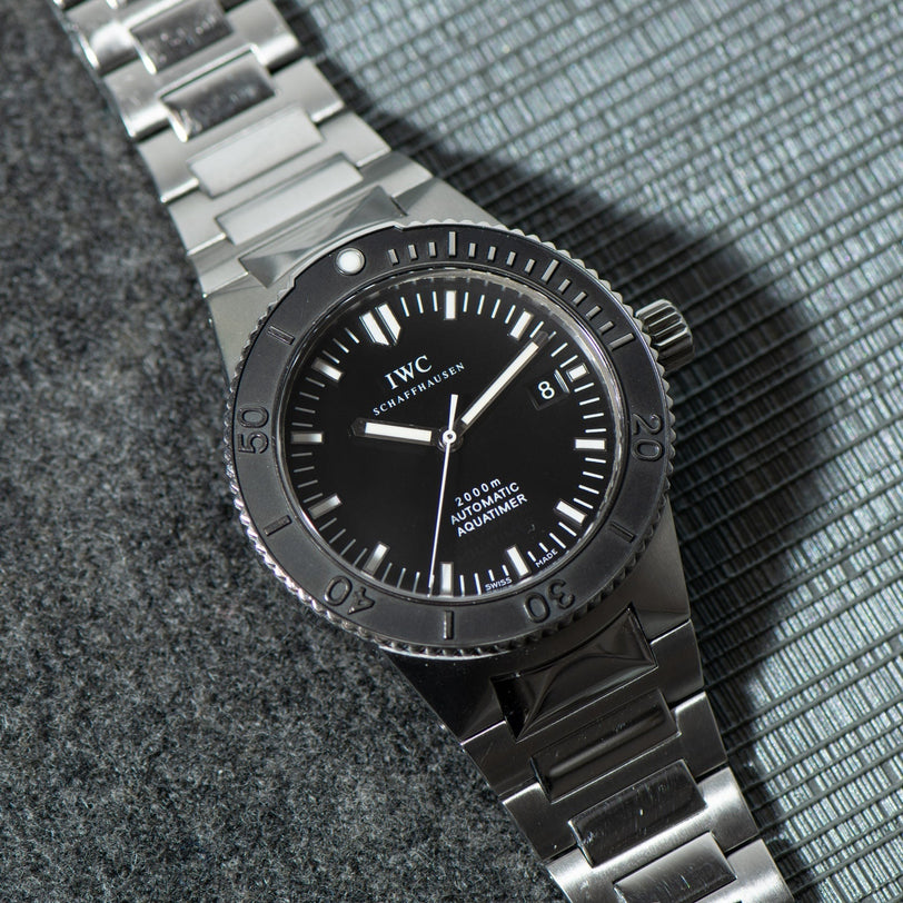 An IWC Schaffhausen Aquatimer GST 2000 stainless steel wristwatch with black dial and rotating bezel is displayed on a textured grey surface.