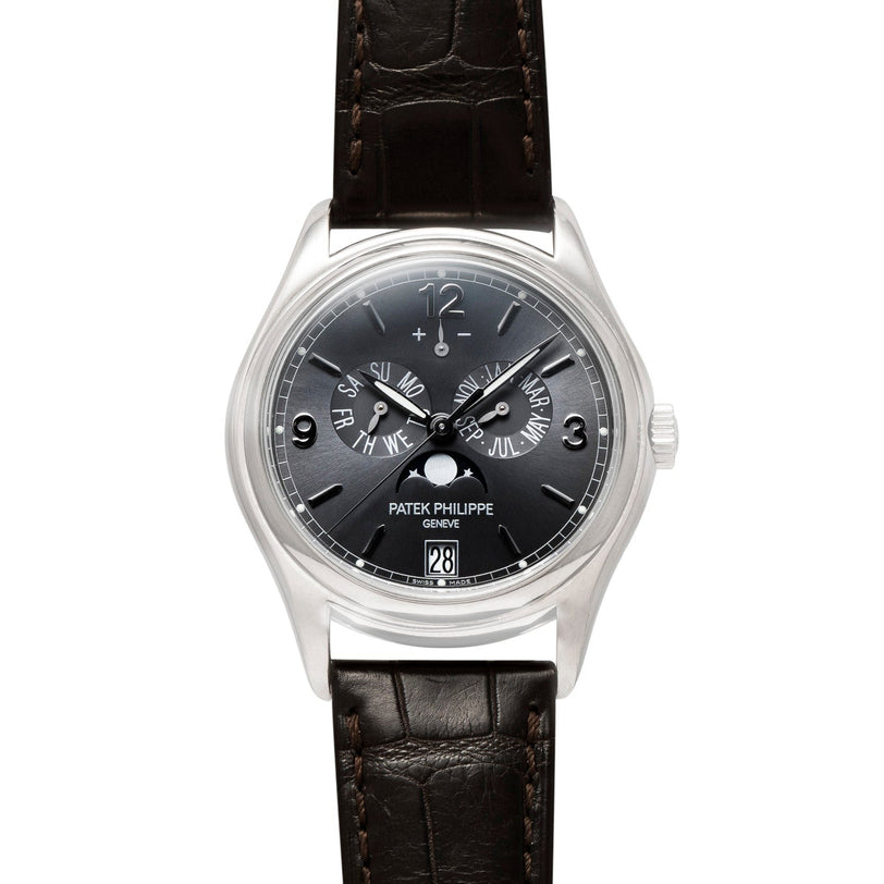 A Patek Philippe Annual Calendar Moonphase wristwatch featuring a black dial, silver case, and brown leather strap.