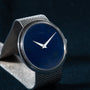 White Gold Lapis by Piaget from Cartier: a white gold mesh watch with a blue lapis face and silver hands, set against a dark, textured background.