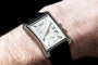 The Piaget Black Tie Emperador Coussin Automatique with a silver dial and black leather strap adorns a wrist.