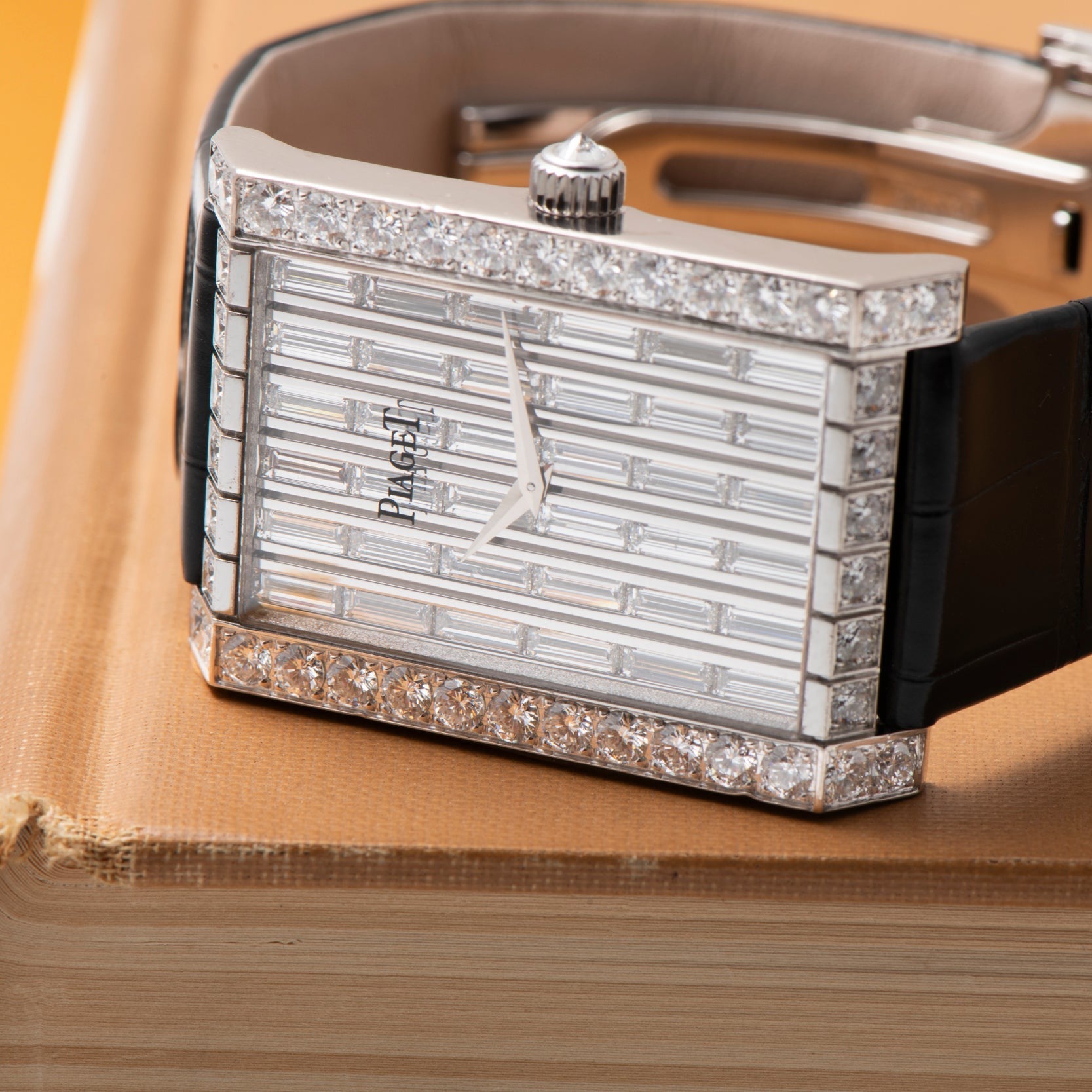 A Piaget Limelight Baguette Diamond Dress Watch with a diamond-encrusted face and black strap rests on a closed book.