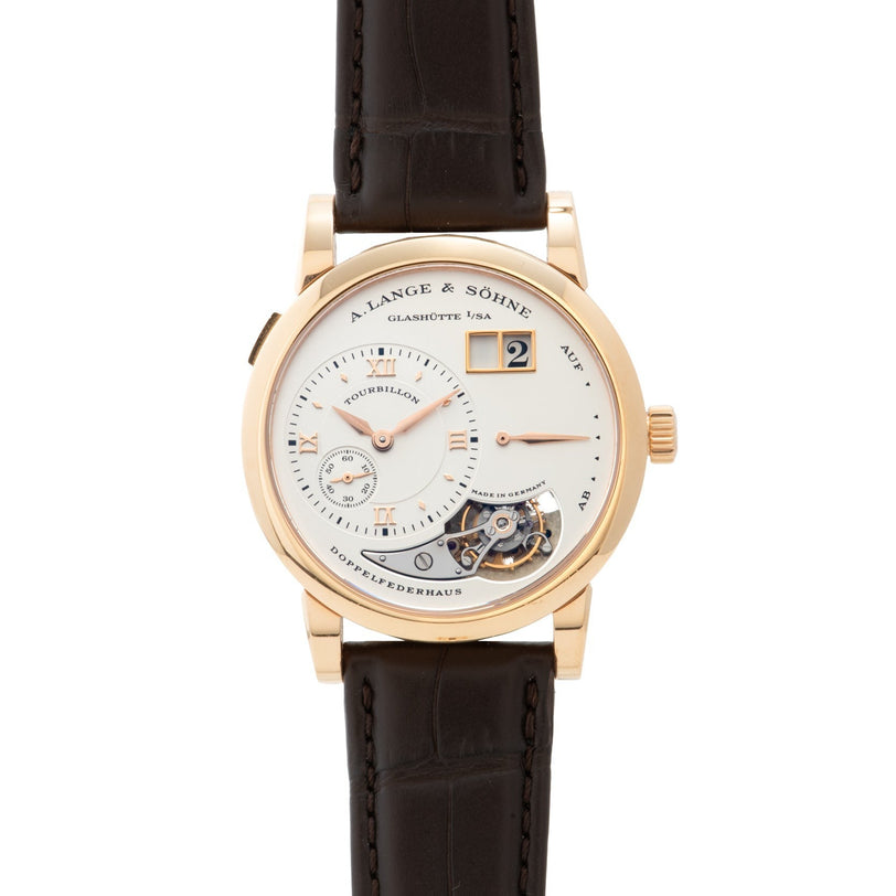 The Lange & Sohne Lange 1 Tourbillon is a luxury wristwatch featuring a brown leather strap and an exposed tourbillon mechanism.