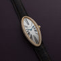 The Cartier Baignoire Allongee, a diamond-encrusted oval watch with a black leather strap, rests on a dark textured surface.