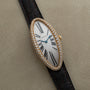 The Cartier Baignoire Allongee features an elongated oval face adorned with diamonds and a black leather strap, displayed on a beige surface.