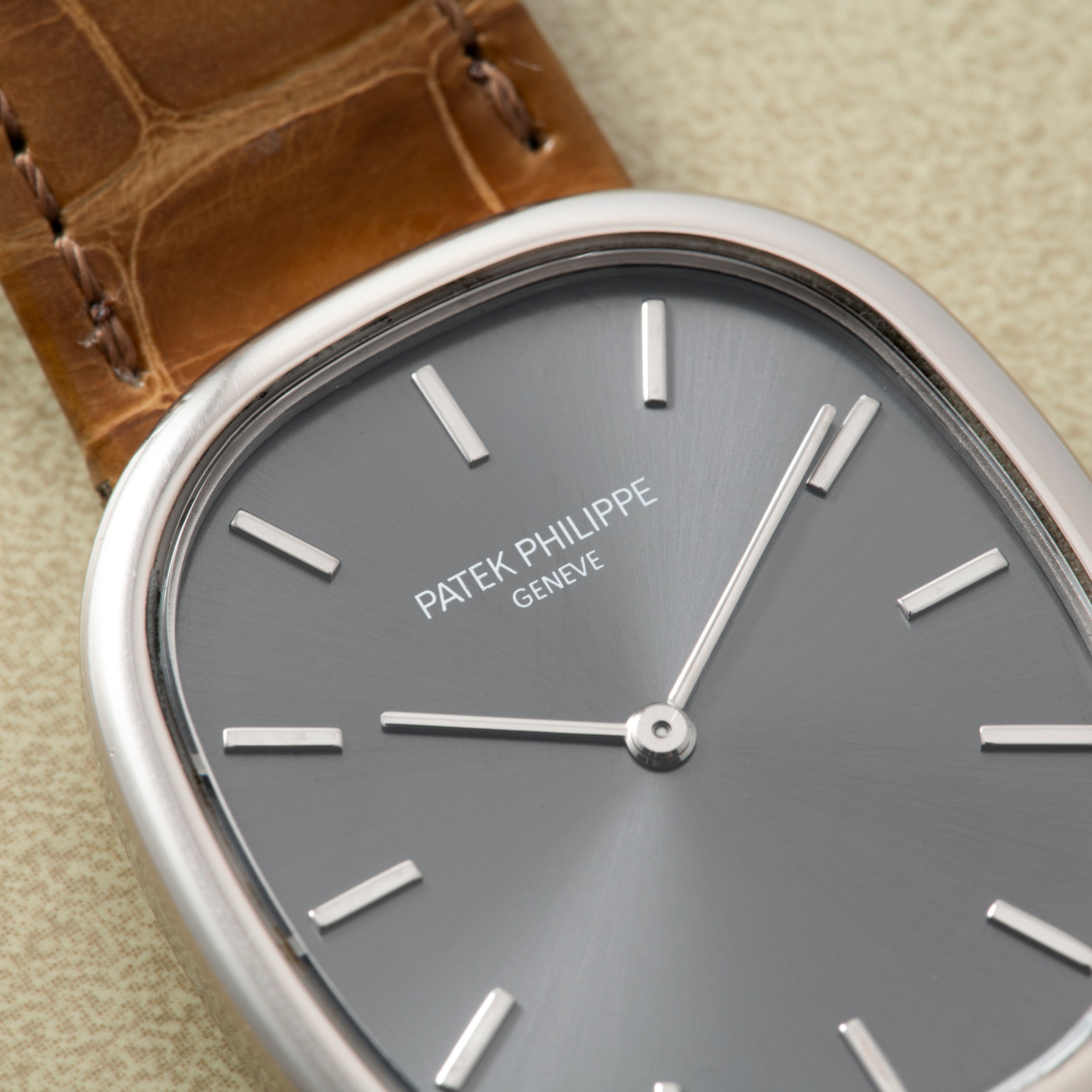 Close-up of the Patek Philippe Ellipse watch featuring a grey face, silver markers, and a brown leather strap.