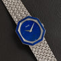 The Piaget Lapis Lazuli White Gold Dress Watch features an octagonal blue face and a woven metal band, displayed on a black leather surface.
