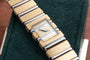 A Piaget Polo Square gold and silver wristwatch with a rectangular face resting on a dark green textured surface.