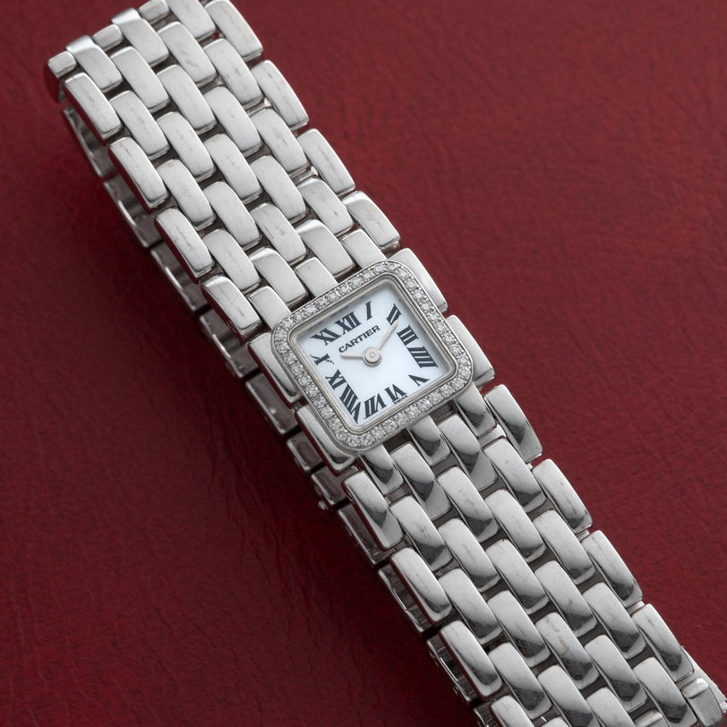 The Cartier Panthère Ruban Mother Of Pearl watch with a square face and Roman numerals rests on a red textured surface.