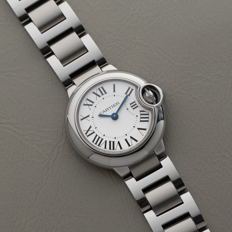 A Cartier Ballon Bleu silver wristwatch featuring Roman numerals, displayed on a grey textured surface.