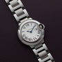 A Cartier Ballon Bleu silver wristwatch with Roman numerals rests on a dark textured surface.