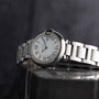 The Cartier Ballon Bleu, a silver wristwatch with Roman numerals and a white dial, rests on a reflective surface.