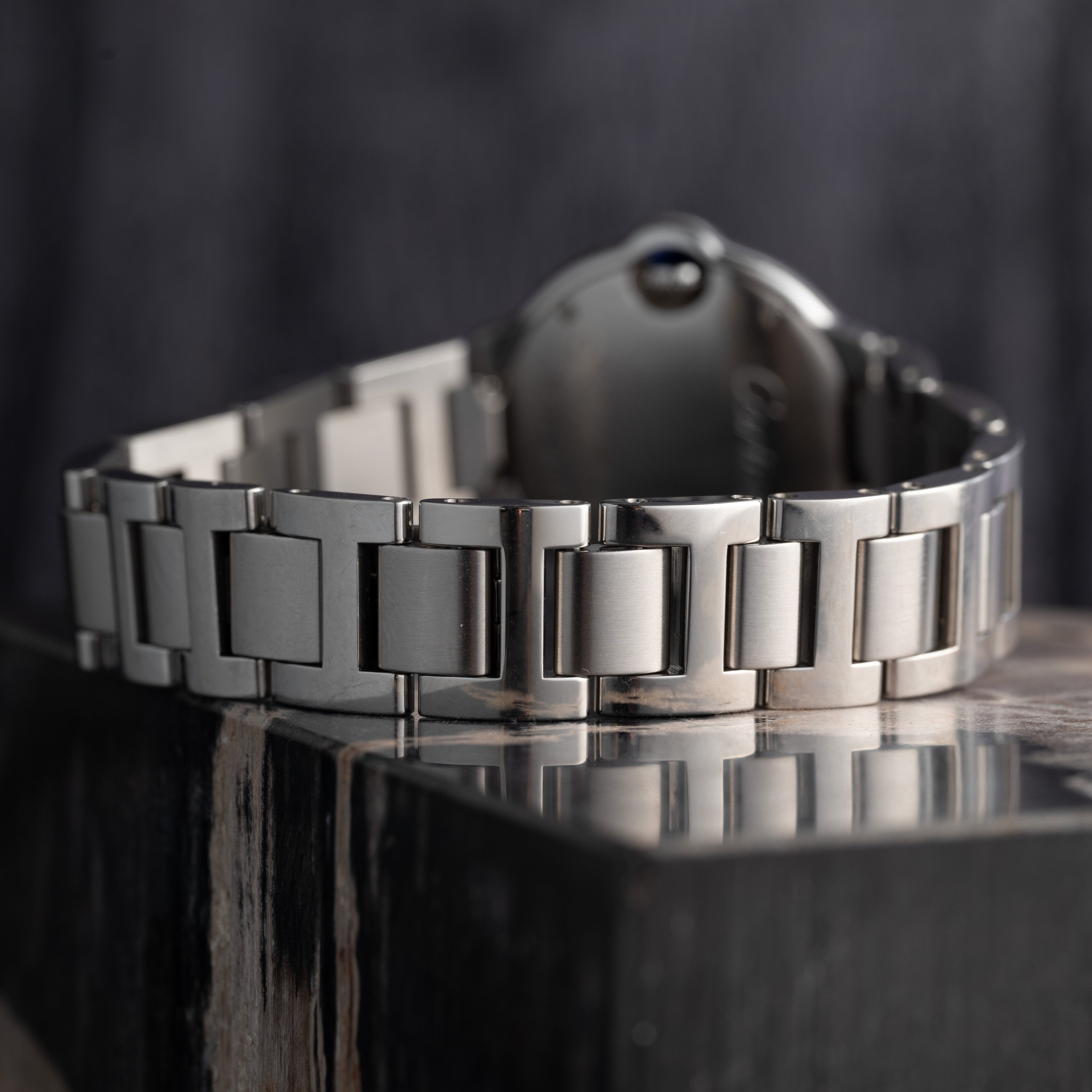 Close-up of the Cartier Ballon Bleus silver metal bracelet resting on a polished, dark stone surface.