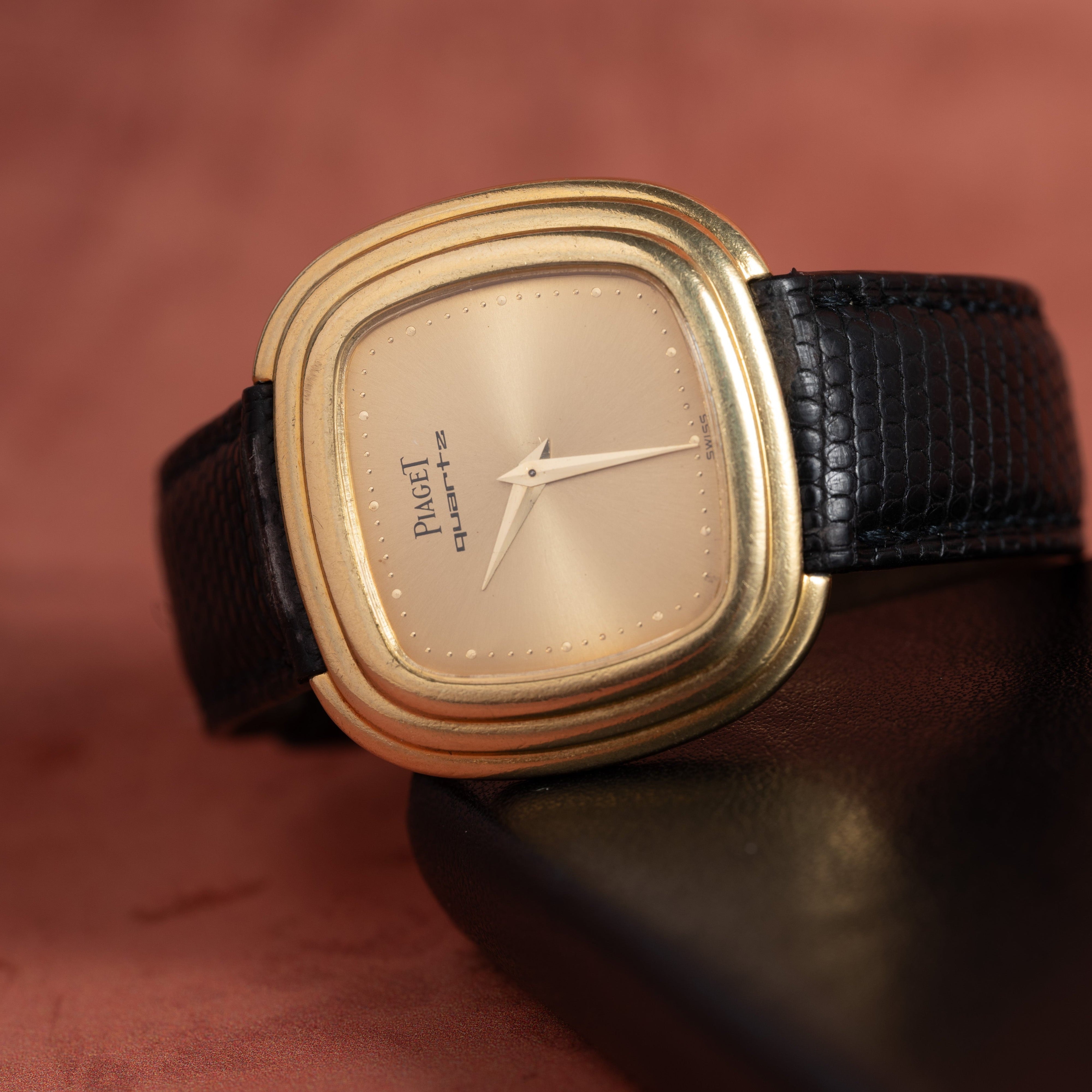 The Piaget Emperador Mini Warhol quartz watch with a black leather strap, displayed on a dark, curved surface.