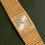 A Piaget Emperador gold quartz watch with a textured band rests on a dark green leather surface.