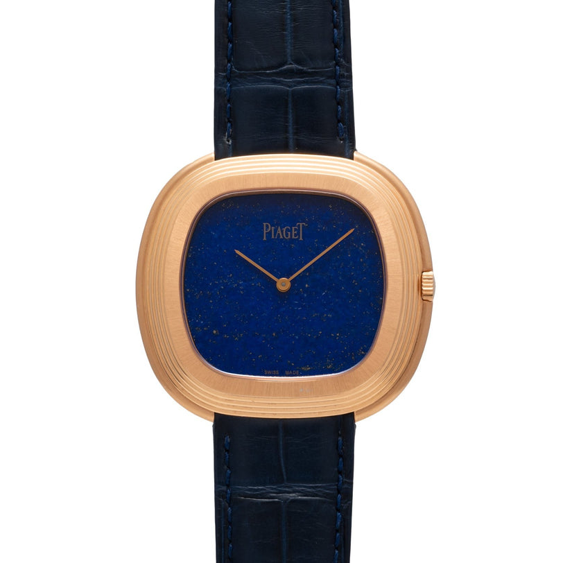 The Piaget Black Tie Andy Warhol watch features a blue lapis lazuli dial, gold case, and black leather strap, shown from the front.