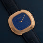A Piaget Black Tie Andy Warhol wristwatch with a blue speckled dial and black leather strap is displayed on a dark surface.