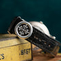 A Patek Philippe Perpetual Calendar Moonphase with a black leather strap and silver clasp, displayed on a yellow metal box.