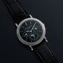 A luxurious black Patek Philippe Perpetual Calendar Moonphase wristwatch with a detailed dial and black leather strap displayed on a dark surface.