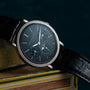 The Patek Philippe Perpetual Calendar Moonphase watch, featuring a black leather strap, rests on a book against a dark background.
