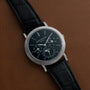 A luxury black Patek Philippe Perpetual Calendar Moonphase wristwatch with a leather strap rests on a brown leather surface.